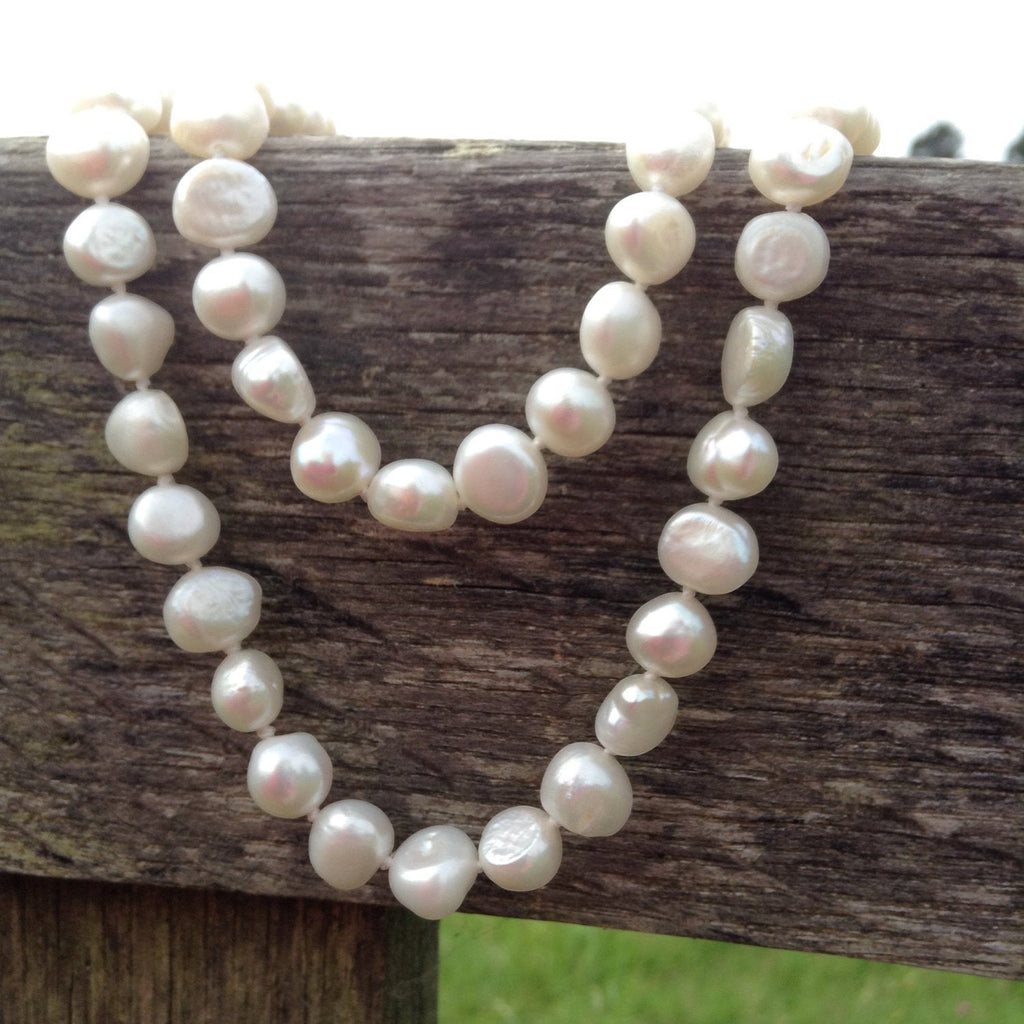 Blue Dragonfly Creations long white baroque freshwater pearl necklace with hand-knotted detailing on a wooden fence.