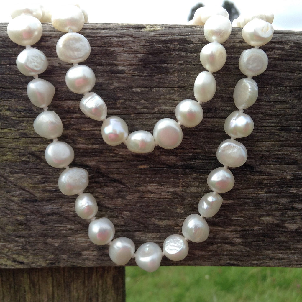 Blue Dragonfly Creations hand-knotted white baroque freshwater pearl necklace draped over a rustic wooden fence.