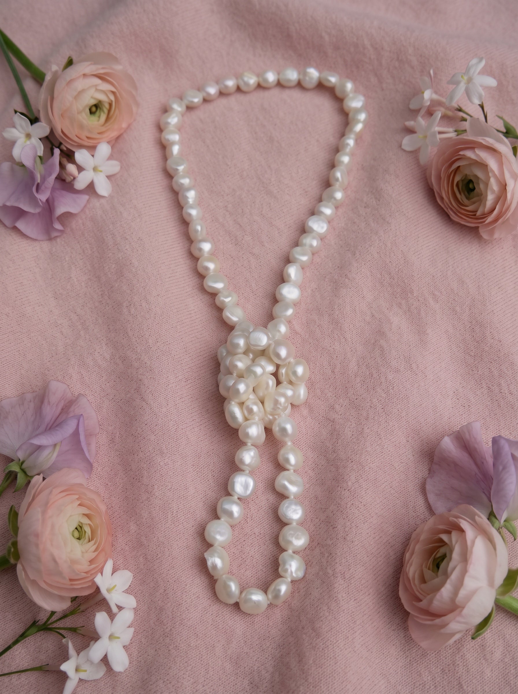 Blue Dragonfly Creations hand-knotted white baroque freshwater pearl necklace on a soft pink fabric background