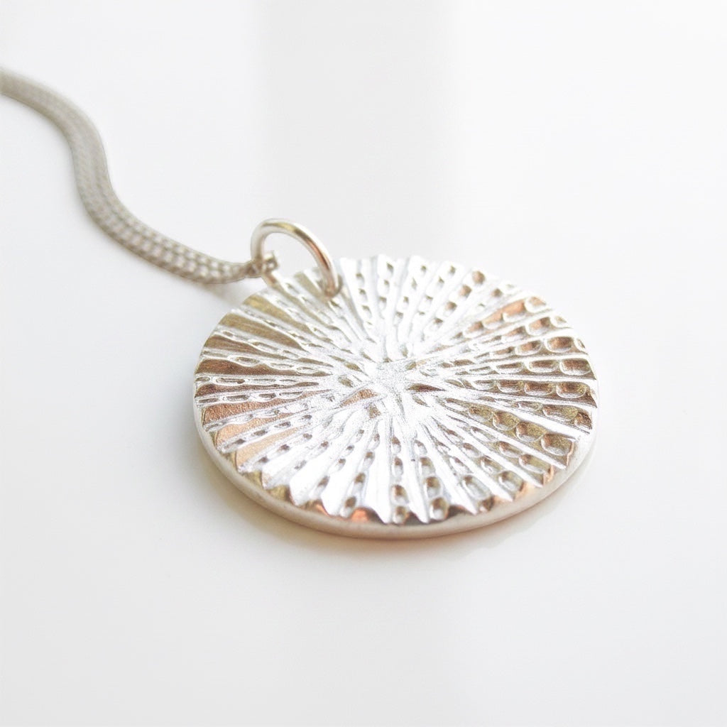 Blue Dragonfly Creations fine silver round pendant necklace with a textured sunburst pattern on a delicate chain.
