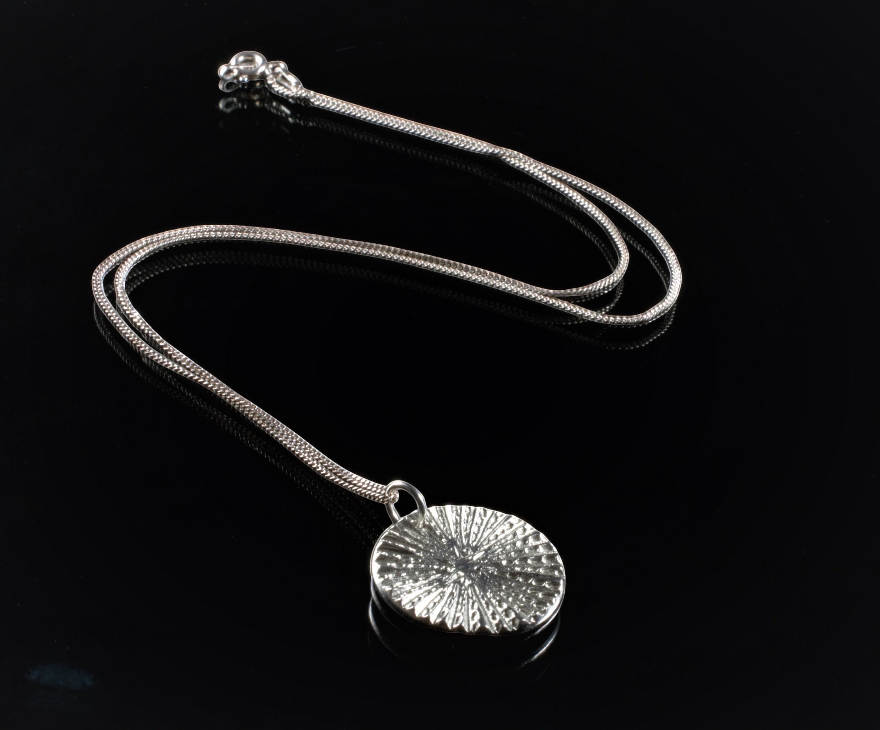 Blue Dragonfly Creations fine silver round pendant necklace with textured radiating lines on a sterling silver chain.