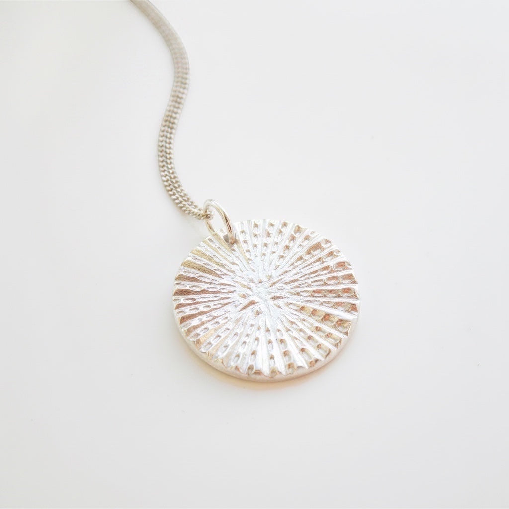 Blue Dragonfly Creations fine silver round pendant necklace with a textured sunburst pattern on a delicate chain.