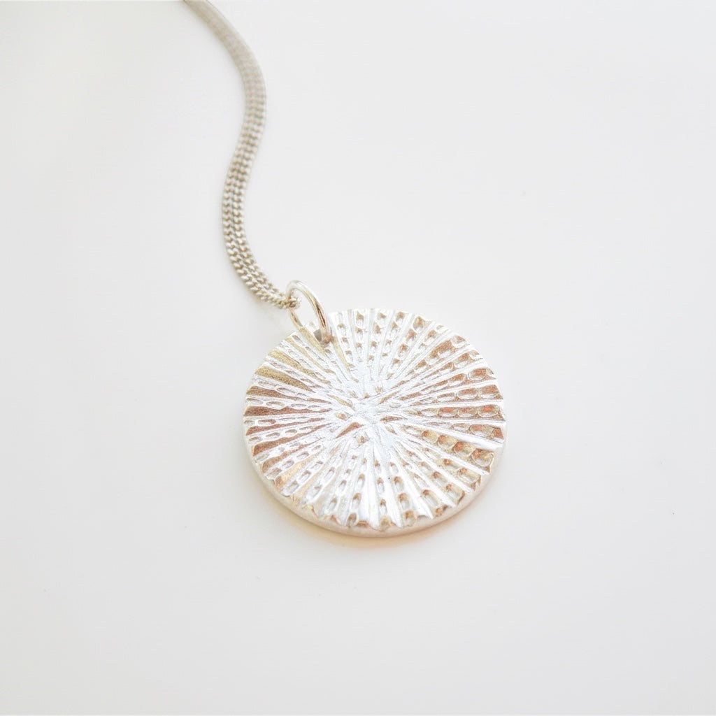 Blue Dragonfly Creations fine silver round pendant necklace with a textured sunburst pattern on a delicate chain.