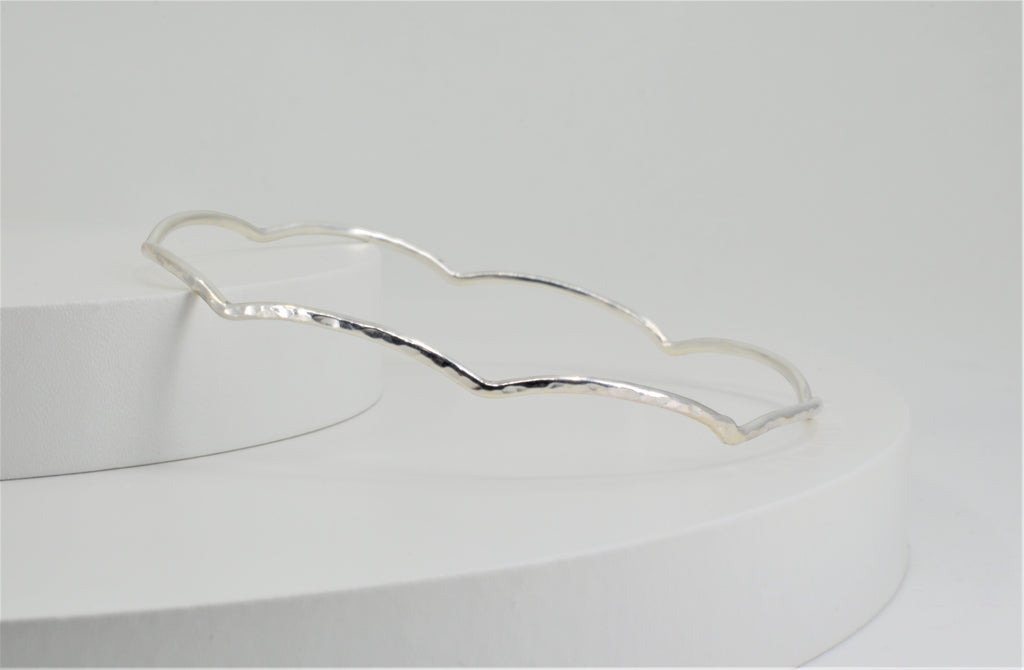 Blue Dragonfly Creations handmade sterling silver bangle with a delicate hammered wave texture on a white display.