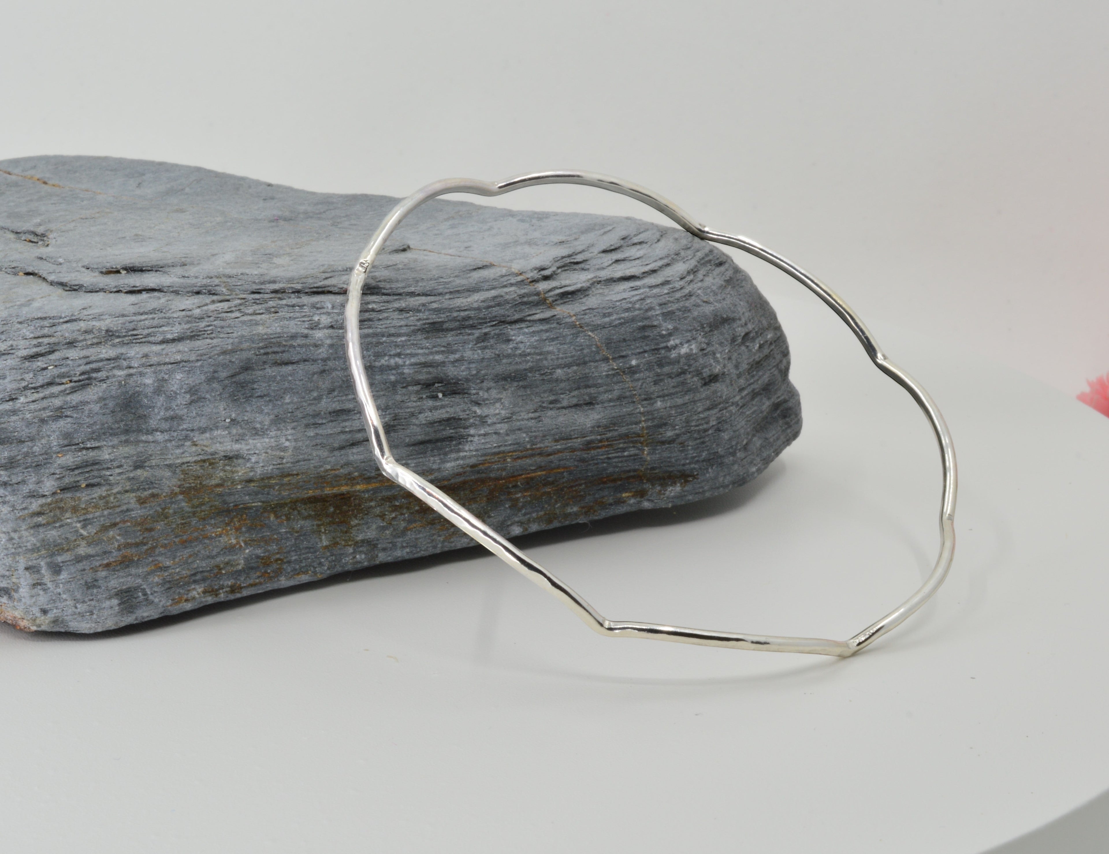 Blue Dragonfly Creations handmade sterling silver bangle with a hammered, wave-textured finish on a grey stone base.