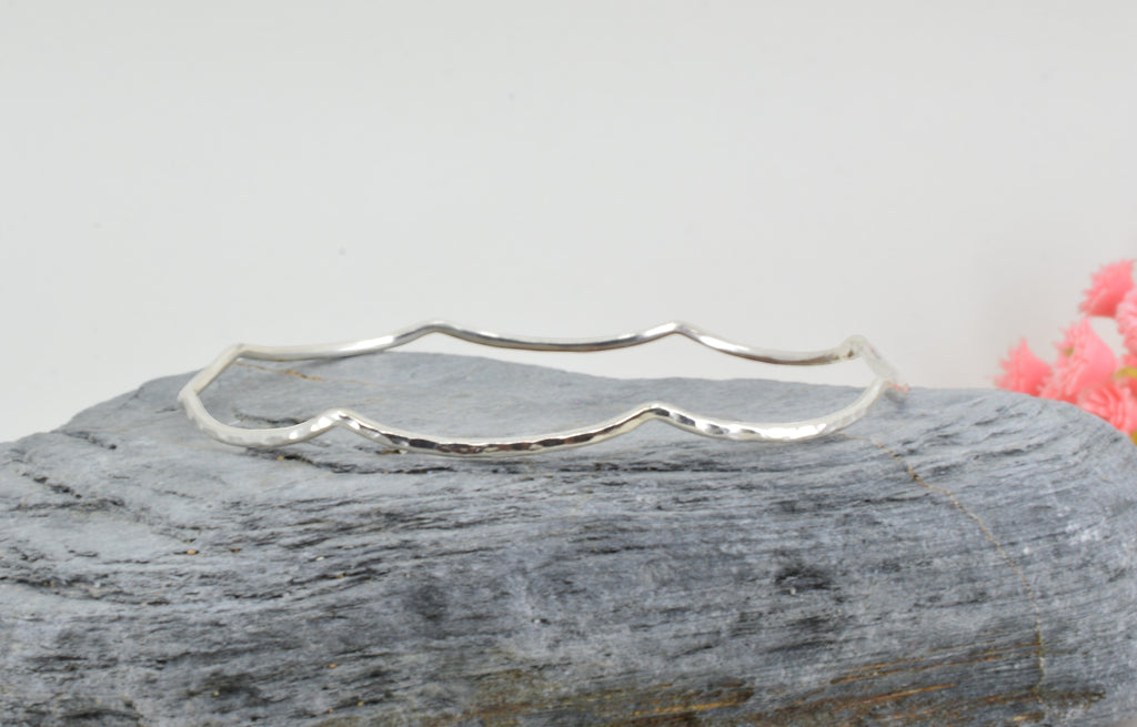 Blue Dragonfly Creations handmade sterling silver bangle with a hammered wave texture on a grey stone surface.