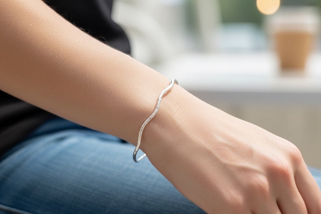 Blue Dragonfly Creations handmade sterling silver bangle with a delicate hammered wave texture on a woman's wrist.