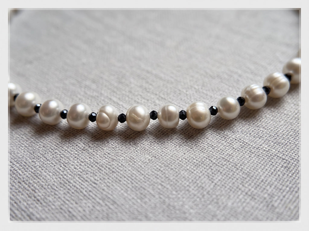 Blue Dragonfly Creations freshwater pearl necklace with white pearls and small faceted black beads on fabric background