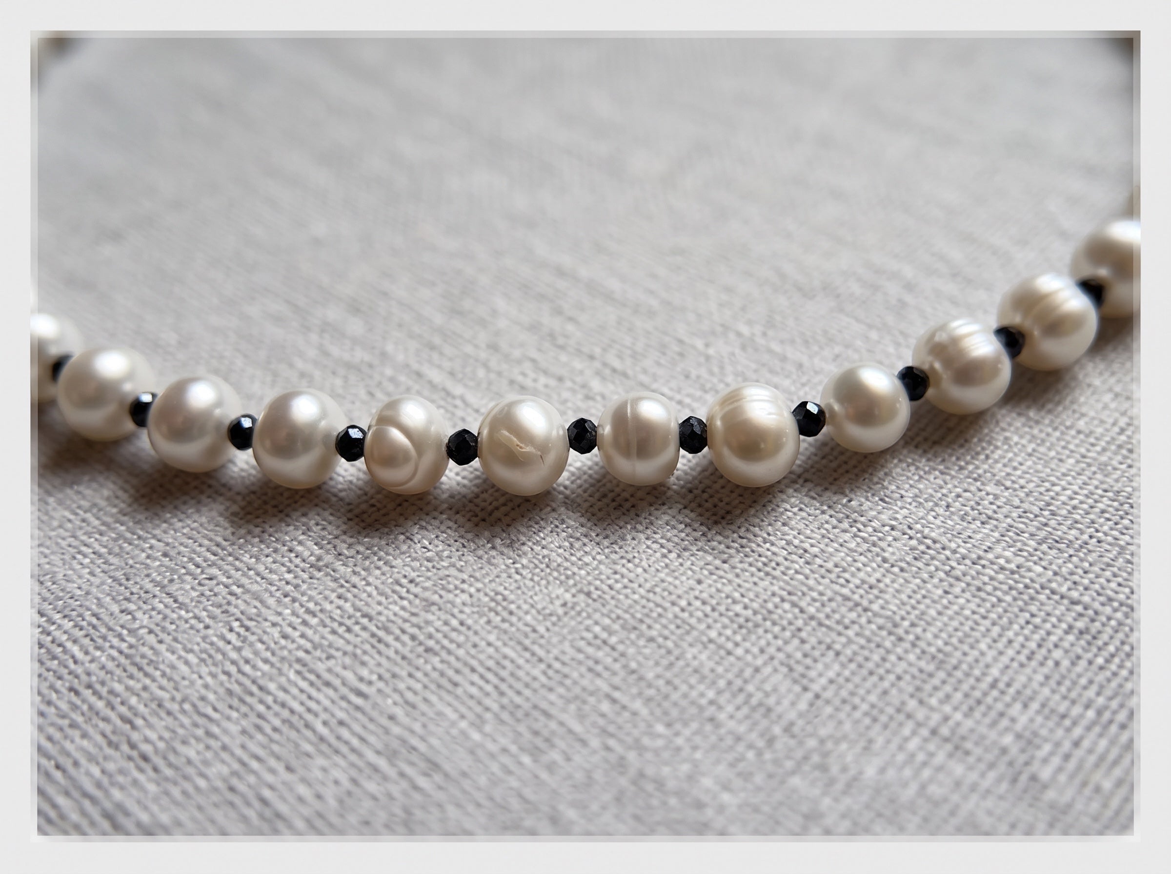 Blue Dragonfly Creations freshwater pearl necklace with white pearls and small faceted black beads on fabric background