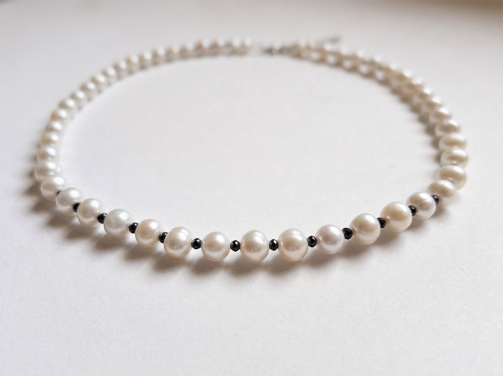 Blue Dragonfly Creations freshwater pearl necklace with white pearls and faceted black beads on a white background.