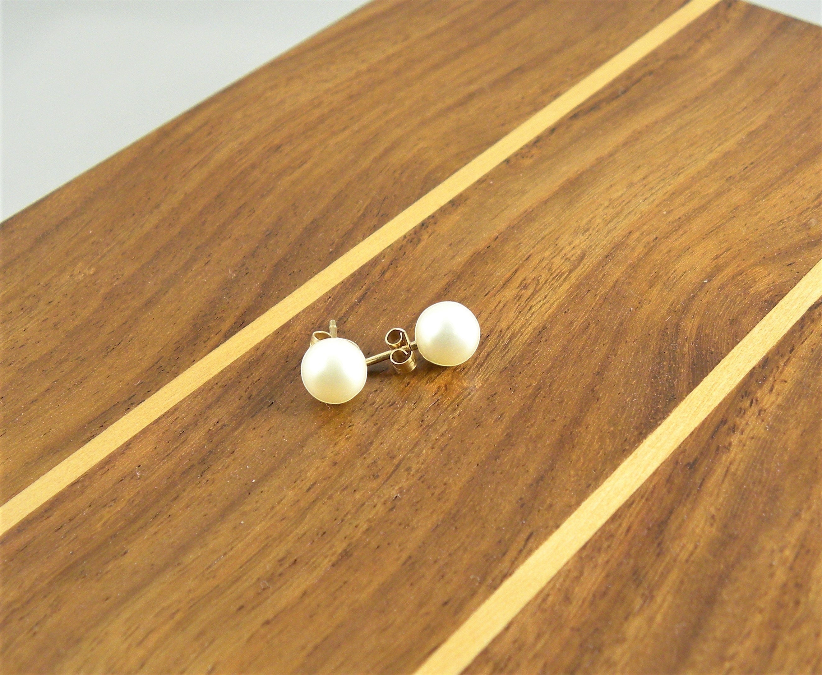 Blue Dragonfly Creations classic round pearl stud earrings with gold-tone posts resting on a wooden surface.