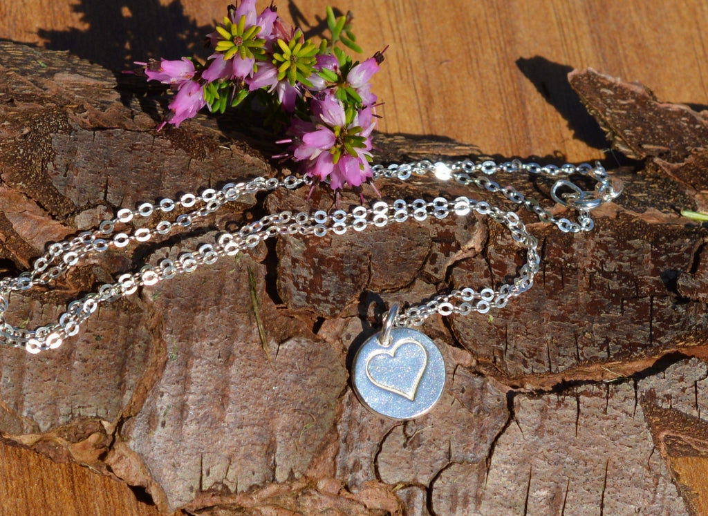 Blue Dragonfly Creations fine silver heart pendant necklace on a 925 sterling silver chain resting on tree bark.