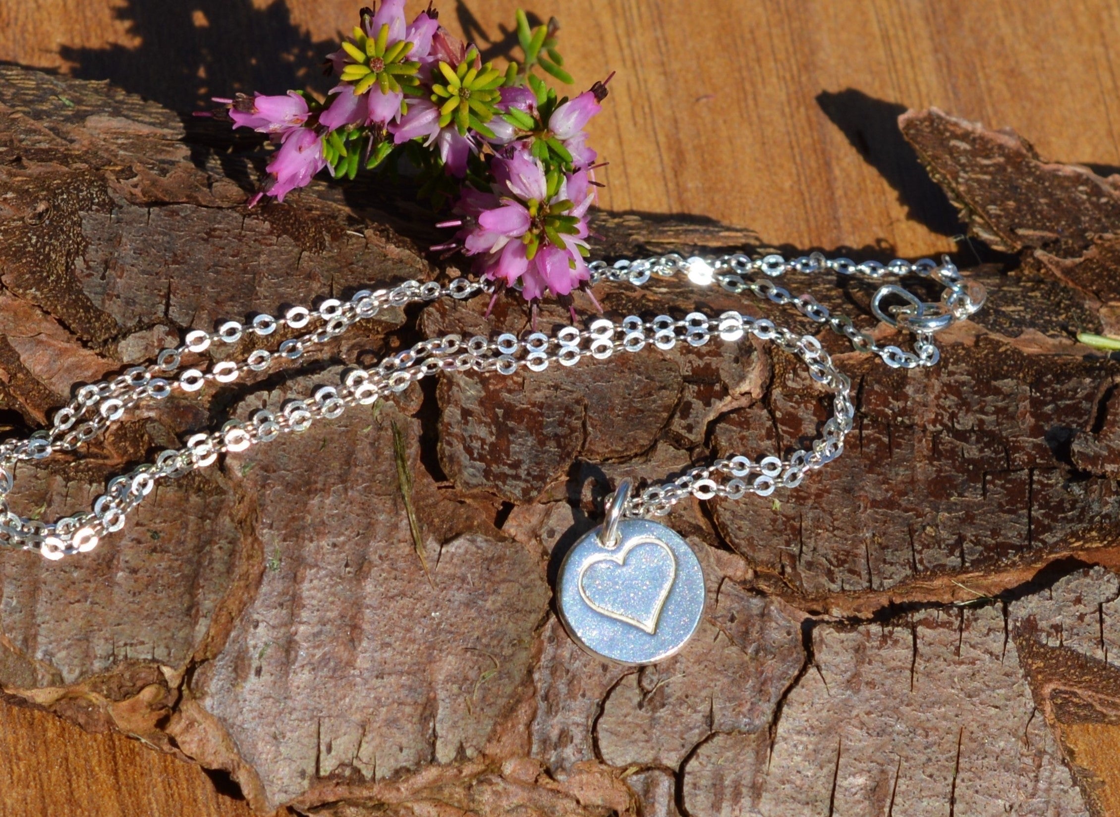 Blue Dragonfly Creations fine silver heart pendant necklace on a 925 sterling silver chain resting on tree bark.